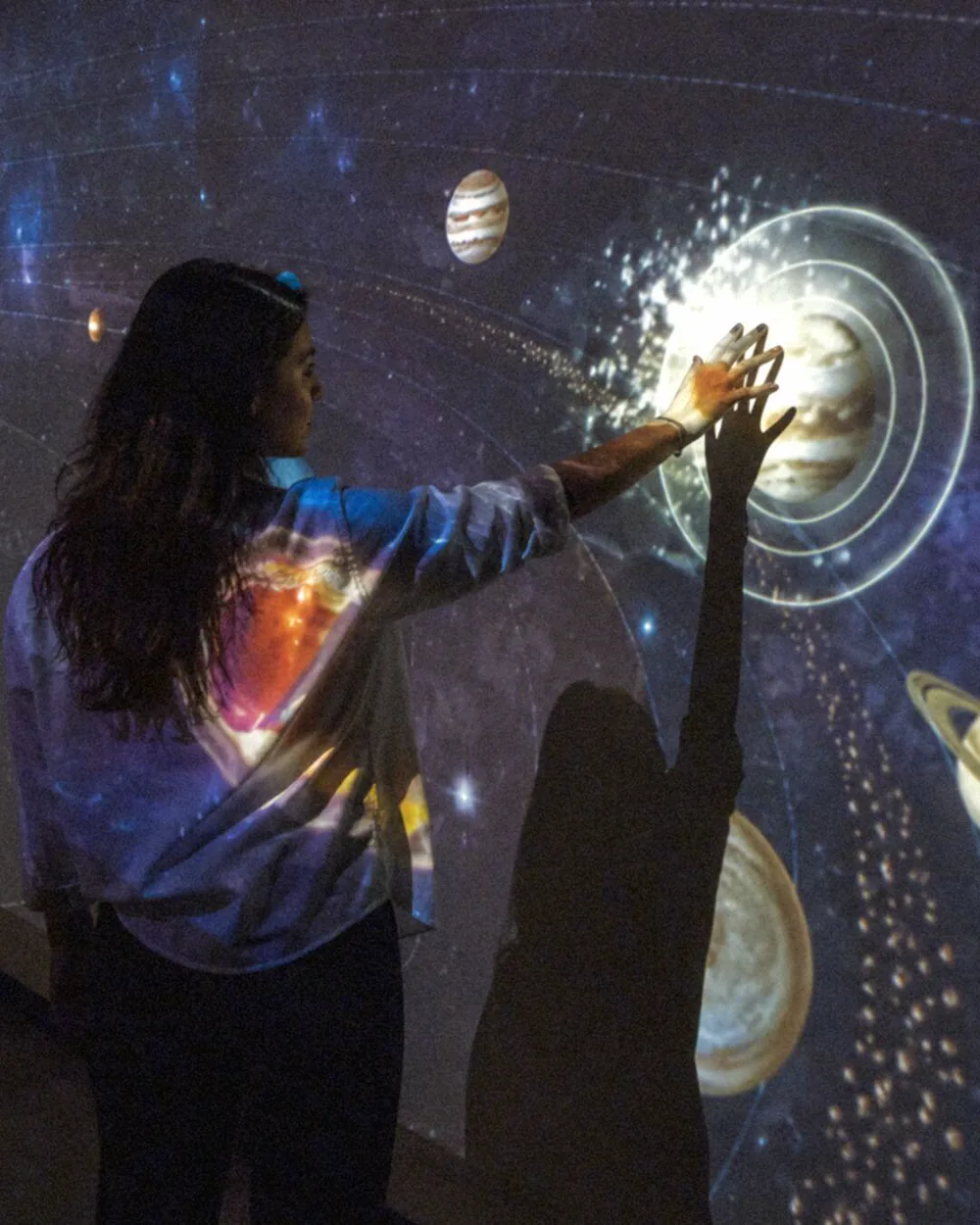 A visitor touching an interactive wall of planets at an activation